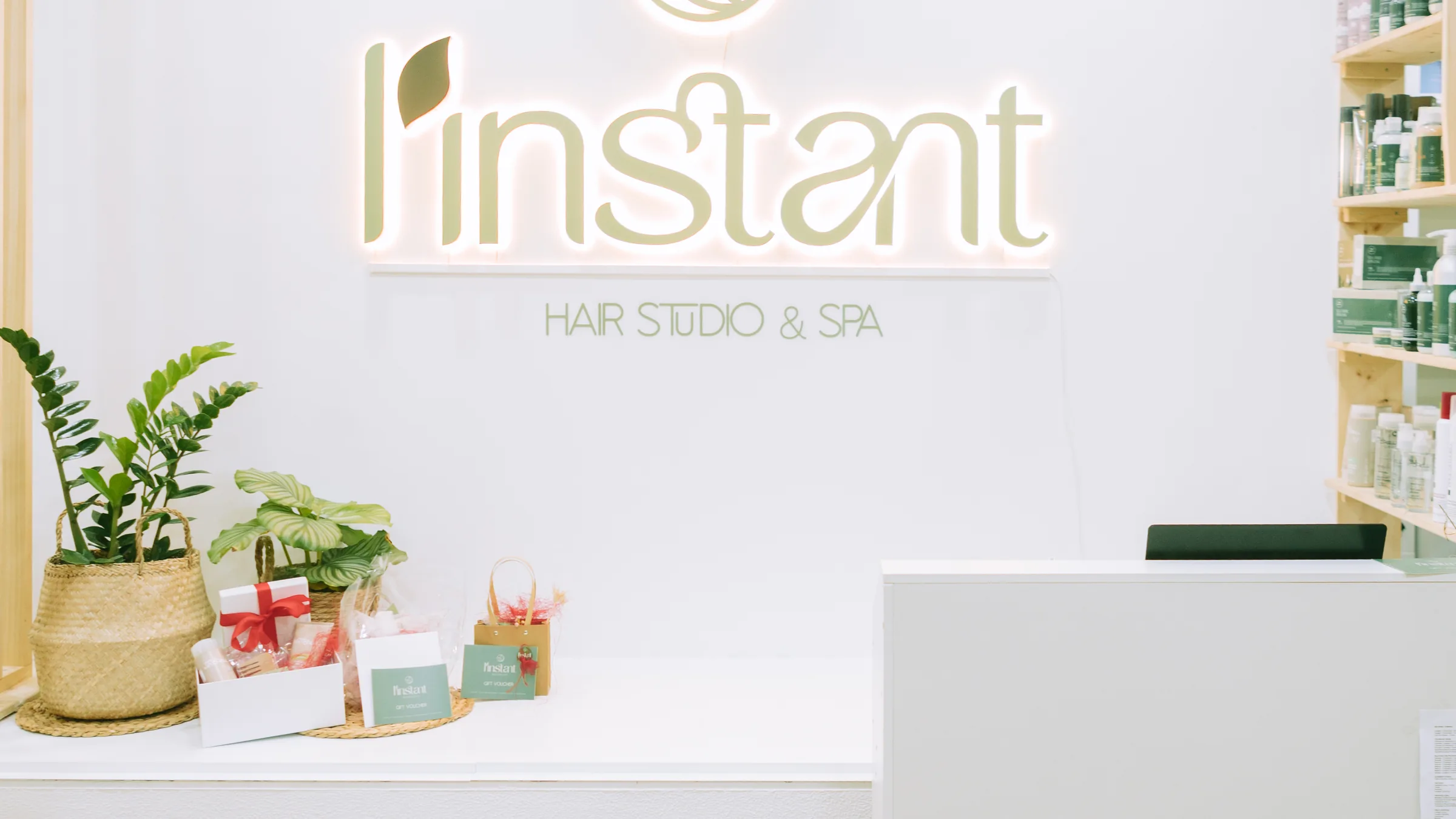 Receção do L'Instant: o letreiro luminoso da marca, plantas e o balcão de atendimento